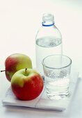 A bottle and a glass of mineral water, apples beside them