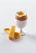 Breakfast egg in egg cup with top removed, pieces of toast