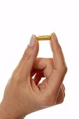 Woman’s hand holding yellow vitamin pill between fingers