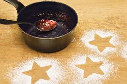 Star shapes outlined in icing sugar and saucepan with jam