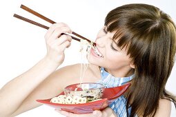 Junge Frau isst asiatisches Nudelgericht mit Essstäbchen
