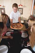 Mann serviert Pizza an einem Tisch mit vier jungen Frauen