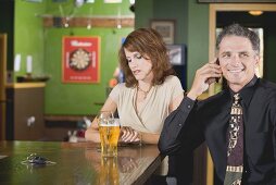 Frau blickt auf die Uhr neben telefonierendem Mann im Pub