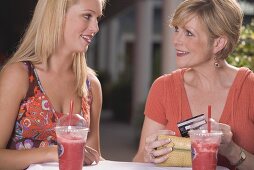 Young woman and mature woman with cold drinks, credit card