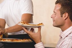 Man with contented expression holding slice of pizza on plate
