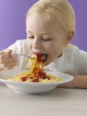 Blondes Mädchen isst Spaghetti mit Tomatensauce