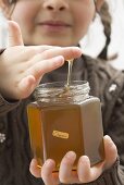 Girl dipping her finger in a jar of organic honey