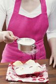 Young woman sprinkling icing sugar over muffins