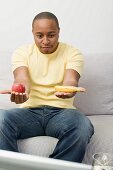 Junger Mann mit Apfel und Banane beim Fernsehen