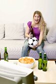Junge Frau mit Fussball und Bierflasche beim Fernsehen