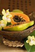 Halved papaya with orchid flowers in wooden bowl