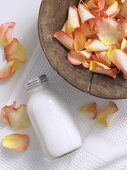 Rose petals in a wooden dish, small bottle of body lotion
