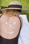 Woman in sun hat with suncream on her back