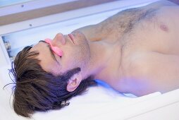 Young man in tanning goggles lying on a tanning bed
