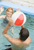 Man and woman playing with beach ball in swimming pool