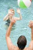 Man and woman playing with beach ball in swimming pool