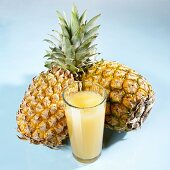 A glass of pineapple juice in front of two whole pineapples