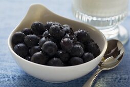 Blueberries in a bowl beside glass of milk