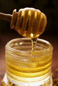 Honey running from honey dipper into honey jar
