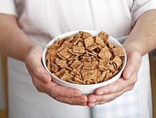 Hände halten Schale mit Frühstücksflakes aus Zimt