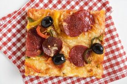 Ein Stück Salami-Pizza mit Paprika und Oliven