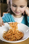 Small girl eating spaghetti with tomato sauce