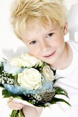 Blond boy holding bouquet of white roses in his hands