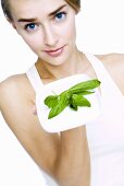 Young woman holding a plate of fresh basil leaves