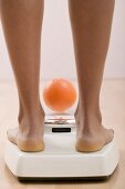 Young woman on bathroom scales with orange