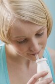 Young, blond woman drinking out of plastic bottle through straw