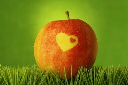 Roter Apfel mit Herz im Gras (grüner Hintergrund)
