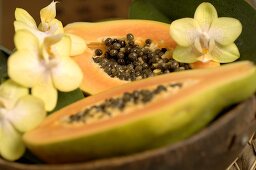 Papaya, halbiert, in Holzschale mit Blüten