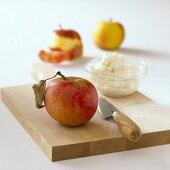 Apple, a dish of quark and a knife on chopping board