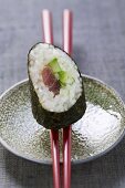 Ein Maki-Sushi mit Thunfisch und Gurke auf Essstäbchen