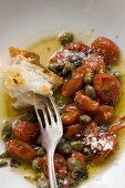Roasted tomatoes with capers, white bread on fork