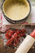Baking tin lined with pastry, redcurrants and rolling pin