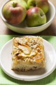 Piece of apple crumble cake, fresh apples in background