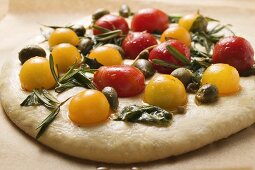 Unbaked pizza with cherry tomatoes, capers & rosemary