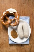 Two cooked Weisswurst with mustard & pretzel on plate