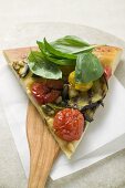 Stück Pizza mit Auberginen, Kirschtomaten und Basilikum