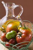Assorted tomatoes in wire basket in front of olive oil