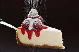 Slice of cheesecake with raspberries, cream, icing sugar on server