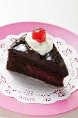 Slice of chocolate cake with cream and cherry on doily