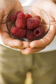 Hands holding small bowl of fresh raspberries