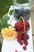 Fresh berries in basket and jar and yellow rose on table