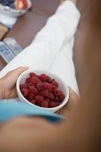 Woman watching TV holding bowl of fresh raspberries