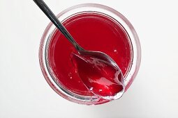 A jar of redcurrant jelly, opened, with spoon