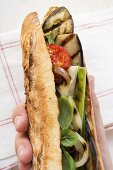 Hand holding grilled vegetables and basil in baguette