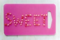 The word 'Sweet' written in sweets on pink chopping board