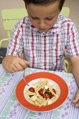 Small boy eating pasta with tomatoes